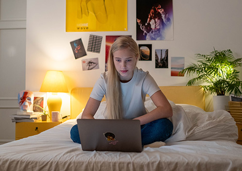 Mädchen sitzt auf Bett mit Laptop